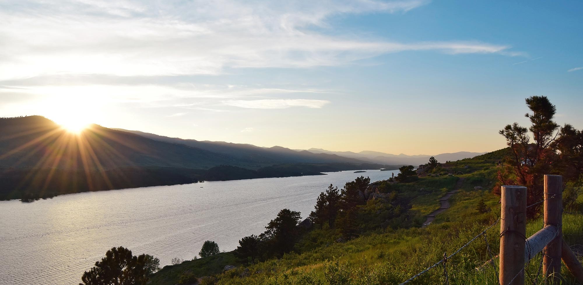 landscape with sun over mountains, water, and rolling hills